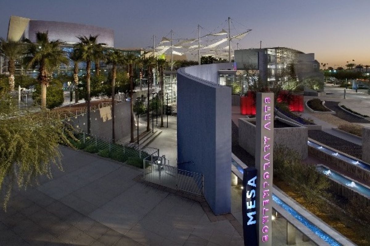 A modern cityscape at dusk with palm trees and a glowing "Mesa Arts Center" sign, perfect for discovering upcoming fall events.