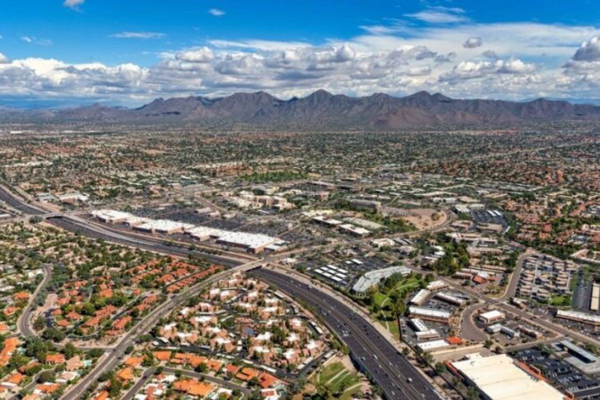 Aerial view of a cityscape—ideal for those relocating to Arizona—with highways, buildings, and distant mountains under a partly cloudy sky.