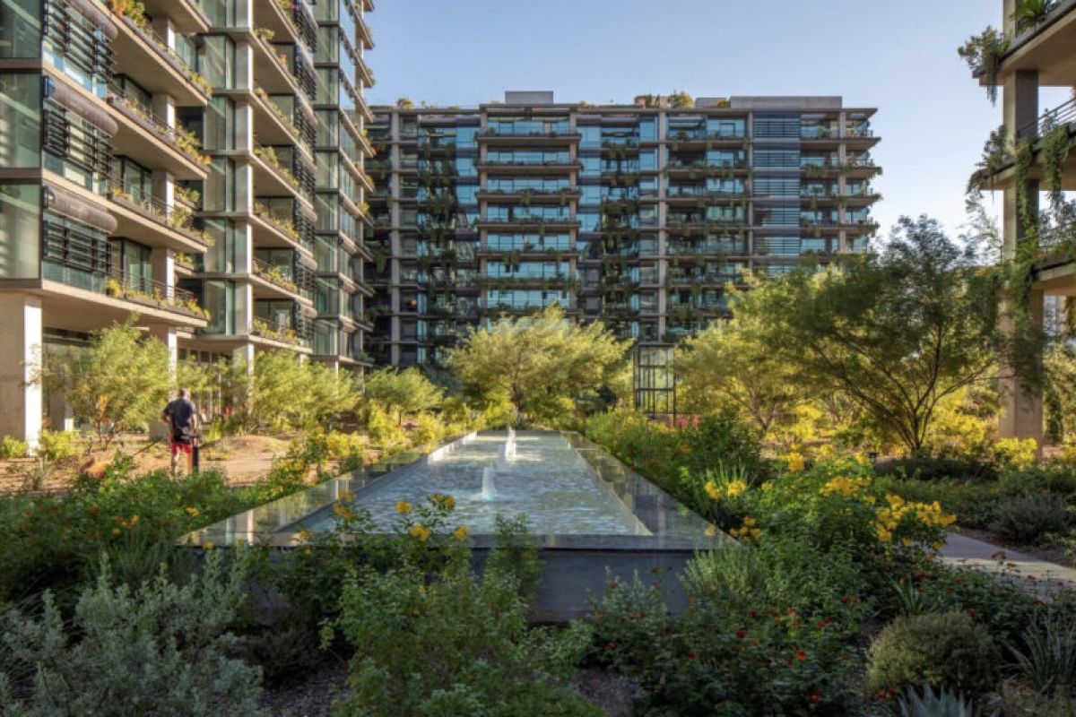 Modern apartment buildings with glass balconies, natural stone accents, lush gardens, and a long reflecting pool in the center.