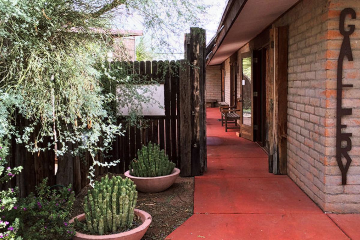 Outdoor walkway with red pavement, cactus plants, and the Hidden Gems of Cattle Track Arts marked by a “GALLERY” sign.