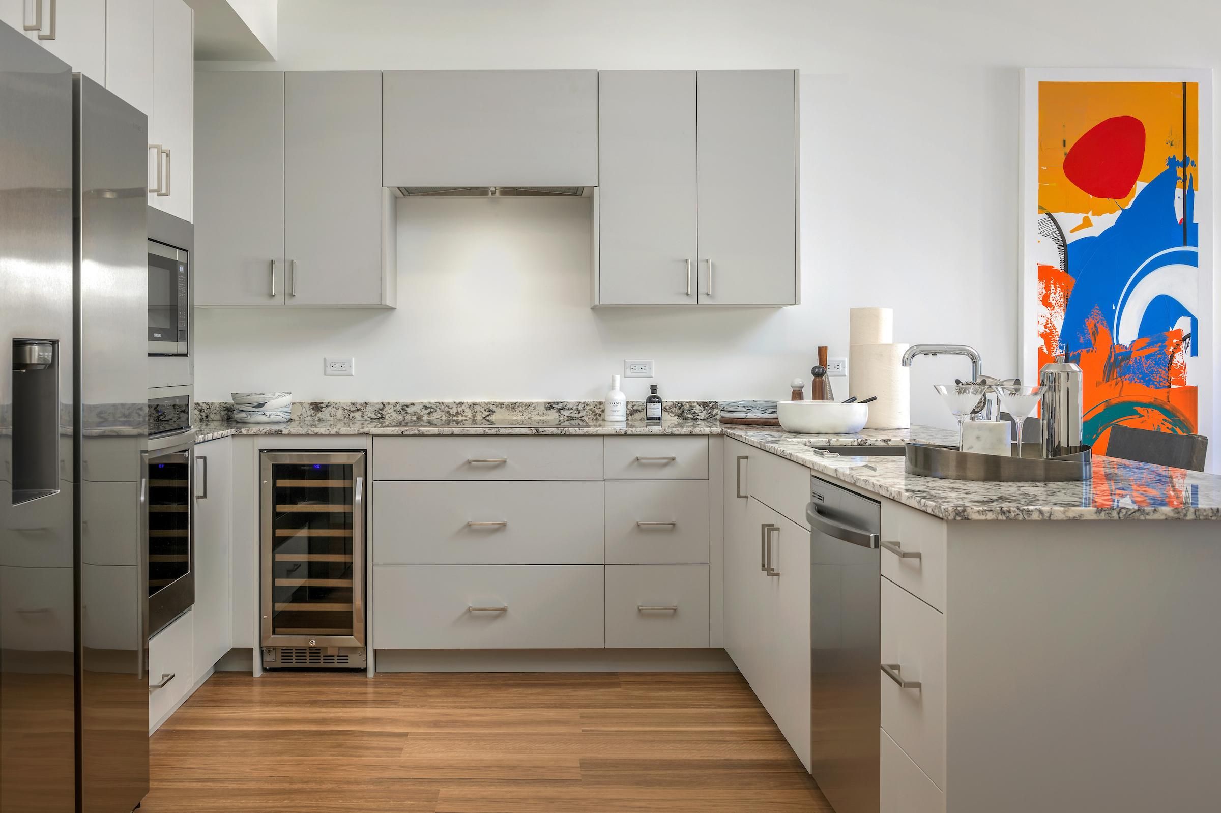 Optima Sonoran Village apartment Modern kitchen with dining table, chairs, barstools, stainless steel appliances, and a plant centerpiece.