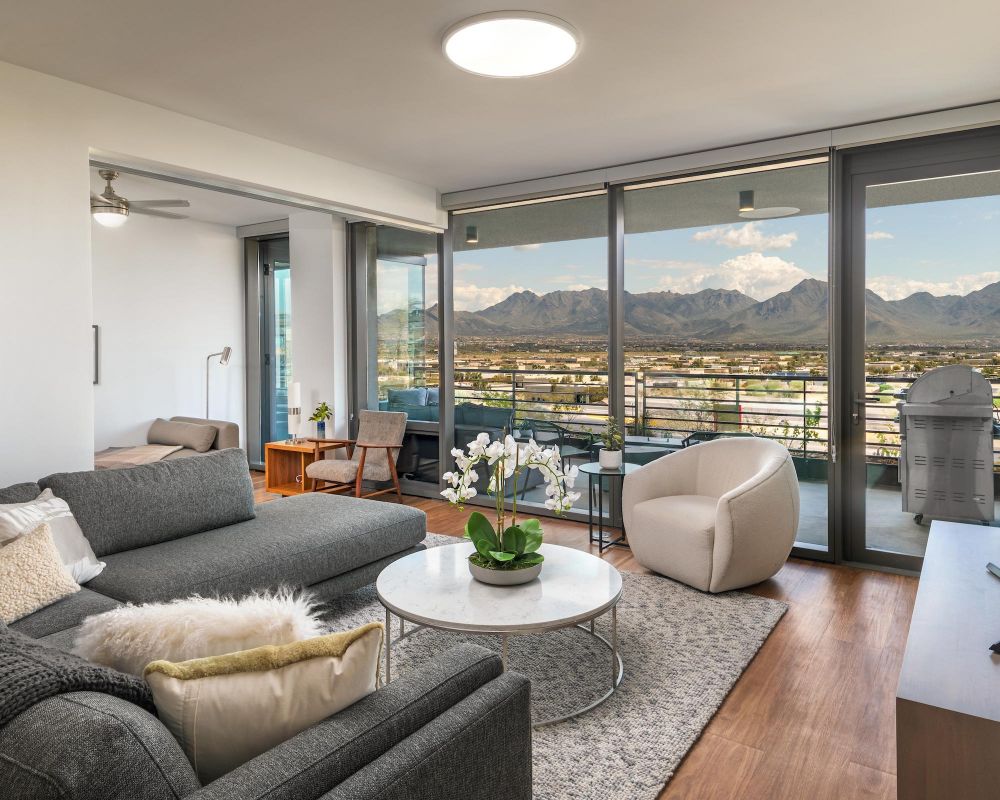 Modern living room with gray sofa, round chair, large windows, and mountain view outside on the balcony.
