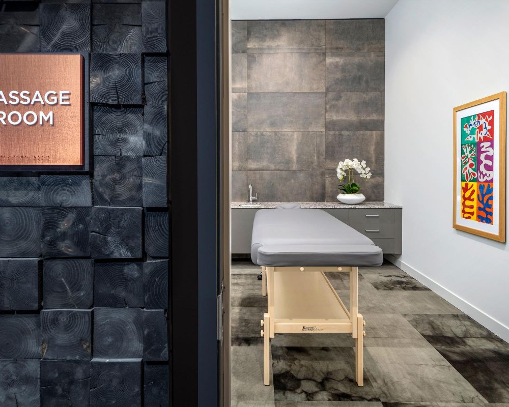 A modern massage room with a massage table, orchid plant, and colorful wall art.