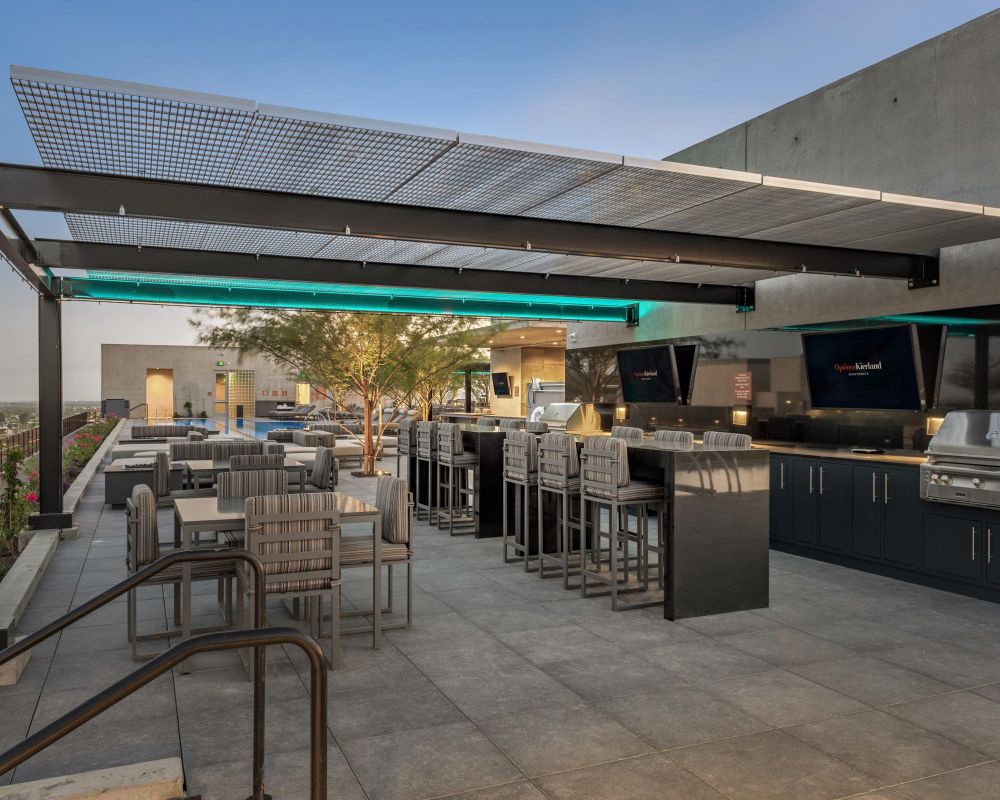 Rooftop patio with dining tables, bar seating, grills, and a modern pergola under a clear sky.