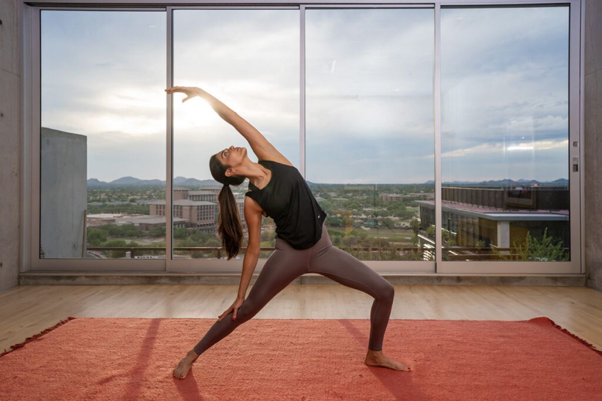 Woman practicing yoga in a modern room, embracing mindfulness as she stretches on a red mat before large windows with a city view.