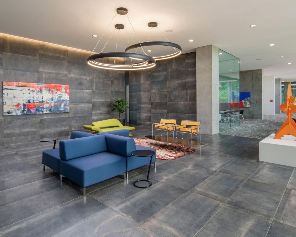 Modern office lobby with blue and green seating, abstract art, sculptures, and large ring ceiling lights.