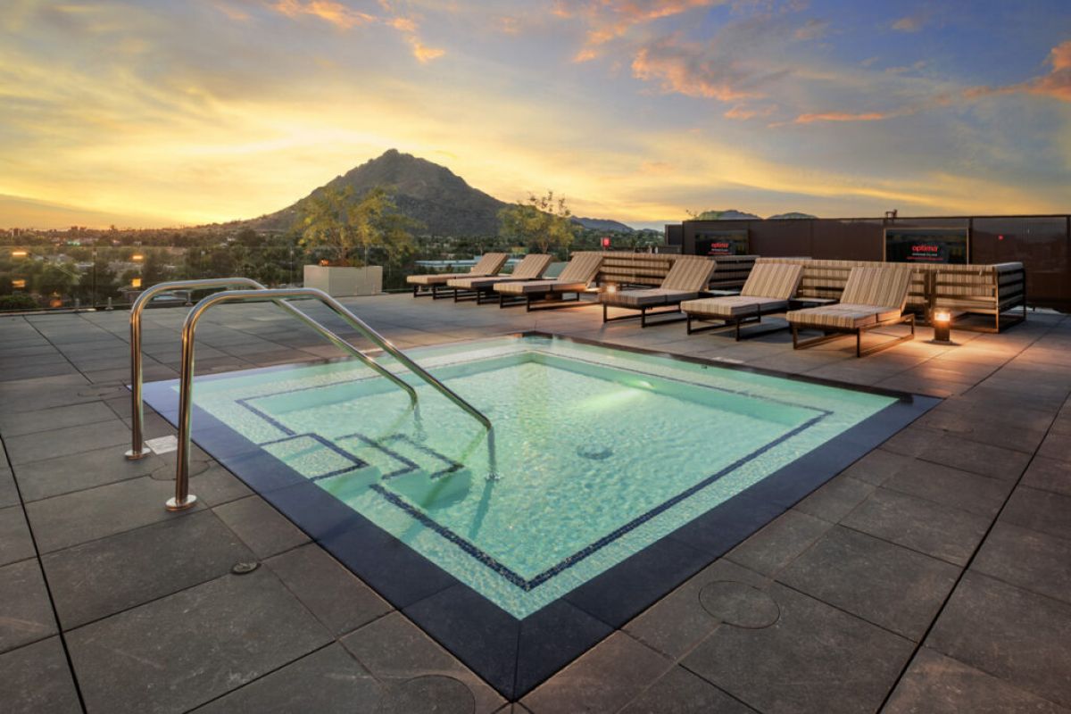 A rooftop hot tub with lounge chairs offers scenic living as it overlooks a mountain at sunset.