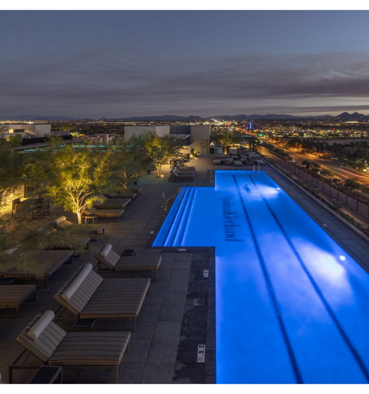 Rooftop pool glowing blue at dusk, with lounge chairs—perfect for Sky Deck evenings amid city lights and distant mountains.