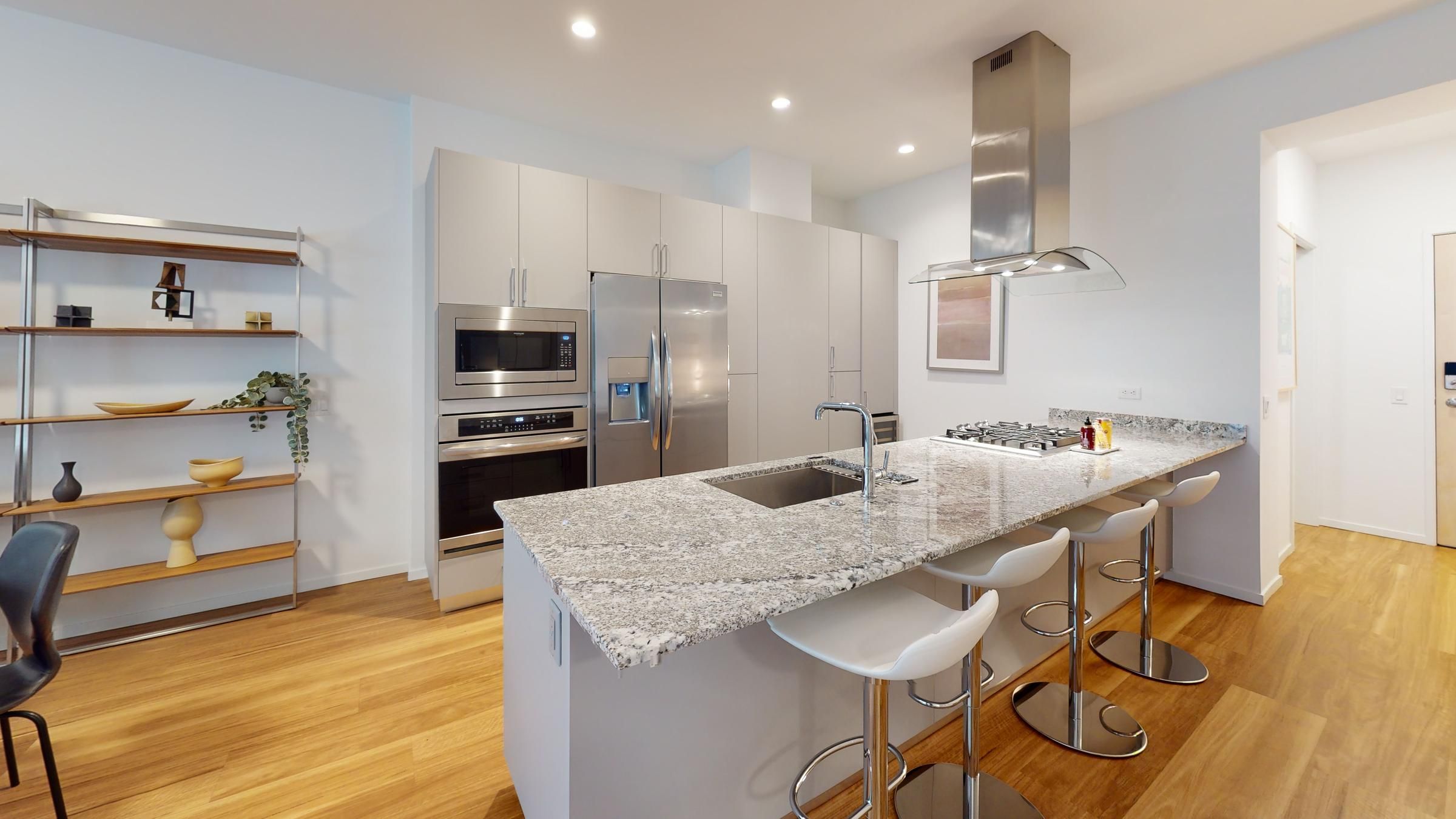 Modern kitchen with granite island, stainless steel appliances, bar stools, and open shelving.