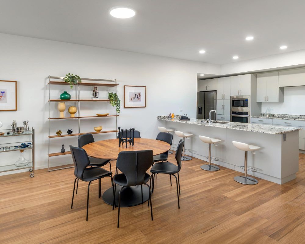 Modern kitchen and dining area with a round table, black chairs, white island, and open shelving.