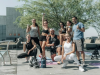 Eight people pose outdoors with dumbbells, showing off Optima Connect perks in stylish athletic wear and bright, ready-for-action smiles.