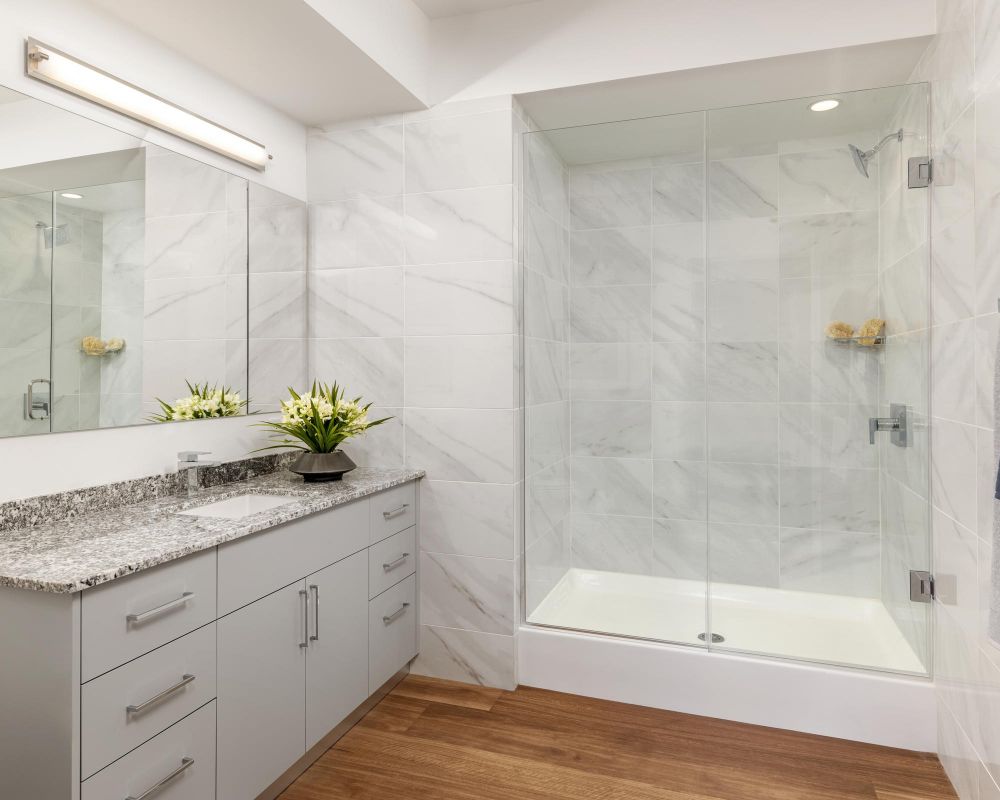 Modern bathroom with marble shower, granite countertop, large mirror, and wooden floor.
