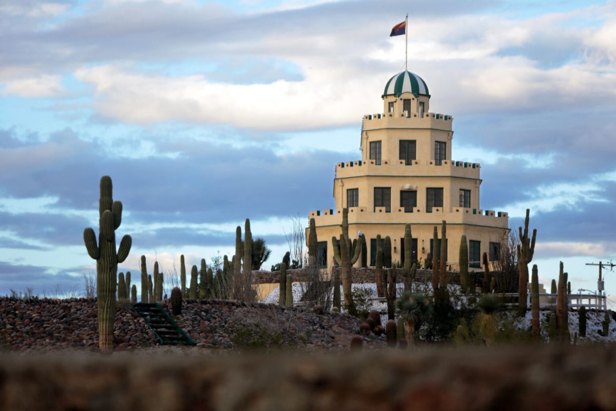 A round, tiered white building with a dome and flag, one of Scottsdale’s architectural treasures, surrounded by cacti under a cloudy sky.