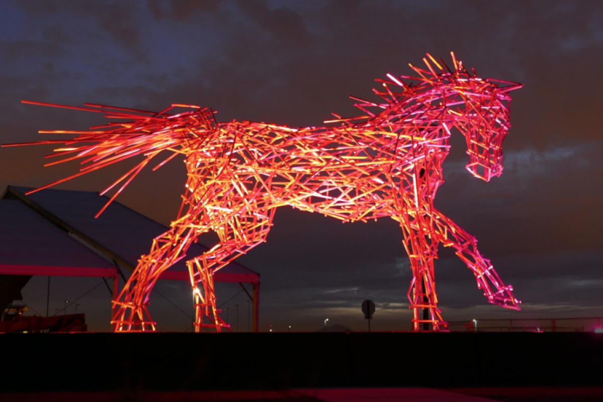 A glowing red horse sculpture, titled Impulsion, shines against a dark sky—an iconic piece from Scottsdale Public Art.