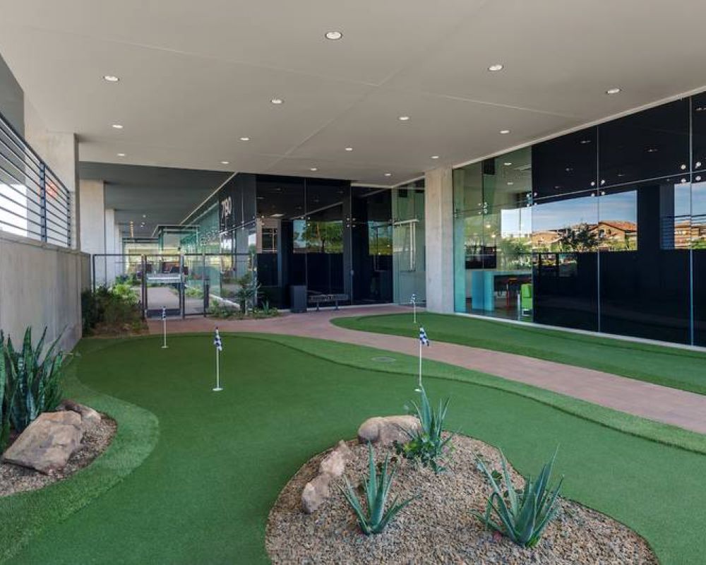Modern indoor putting green with desert plants, rocks, and glass walls reflecting the outdoor scenery.