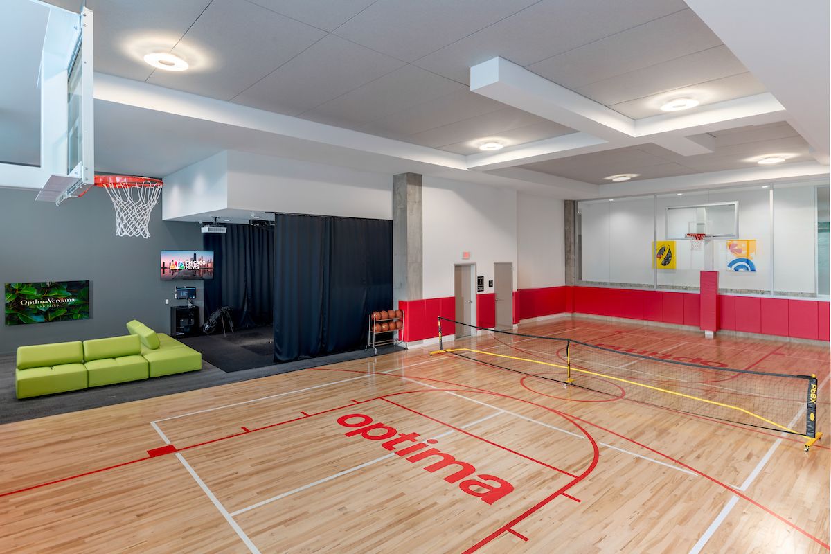 Indoor gym with a basketball court, mini tennis net, green couch, TV, and red accents on the walls and floor.