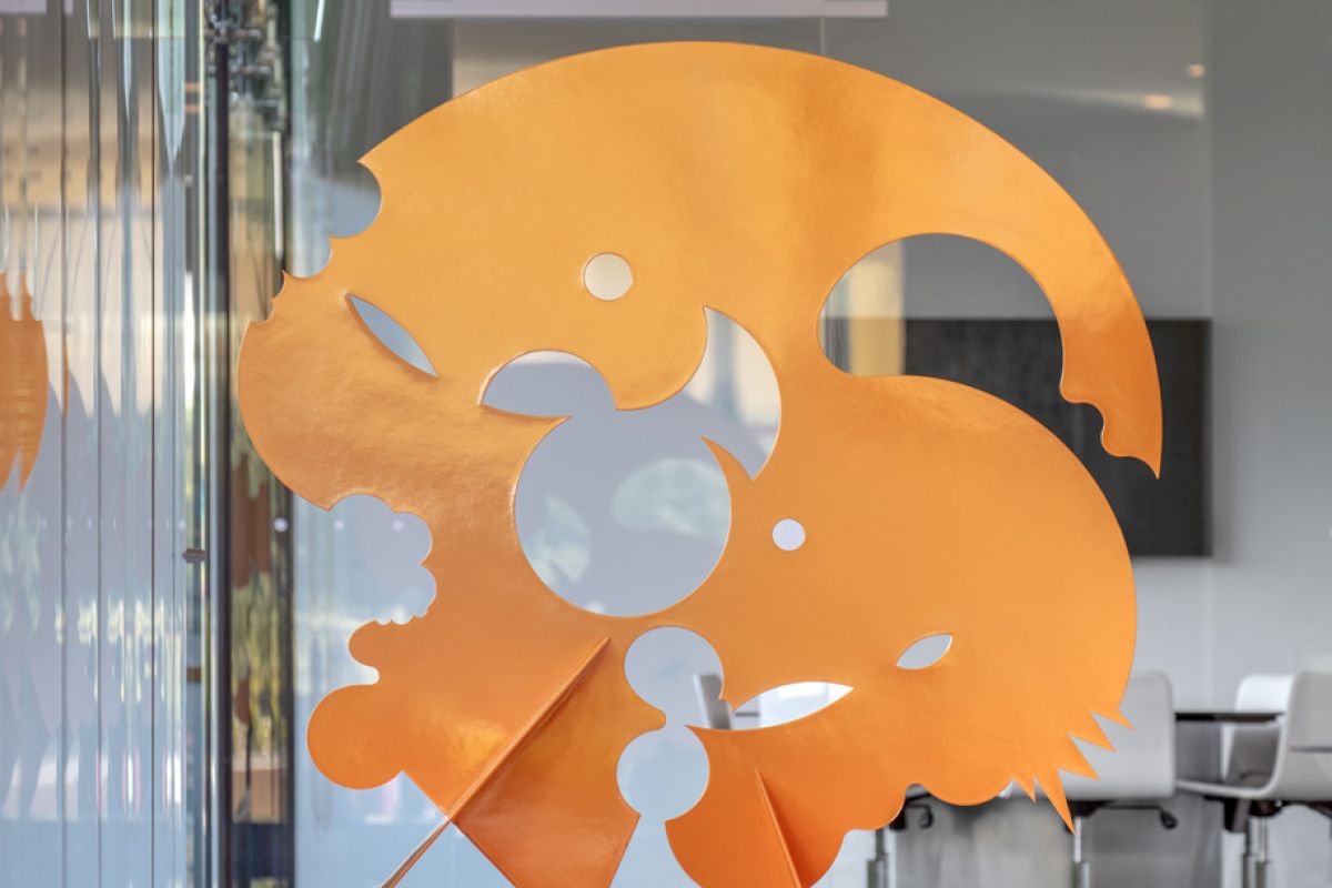 Striking orange abstract sculpture on a dark base adds bold art to a modern office, inspiring creativity and community.