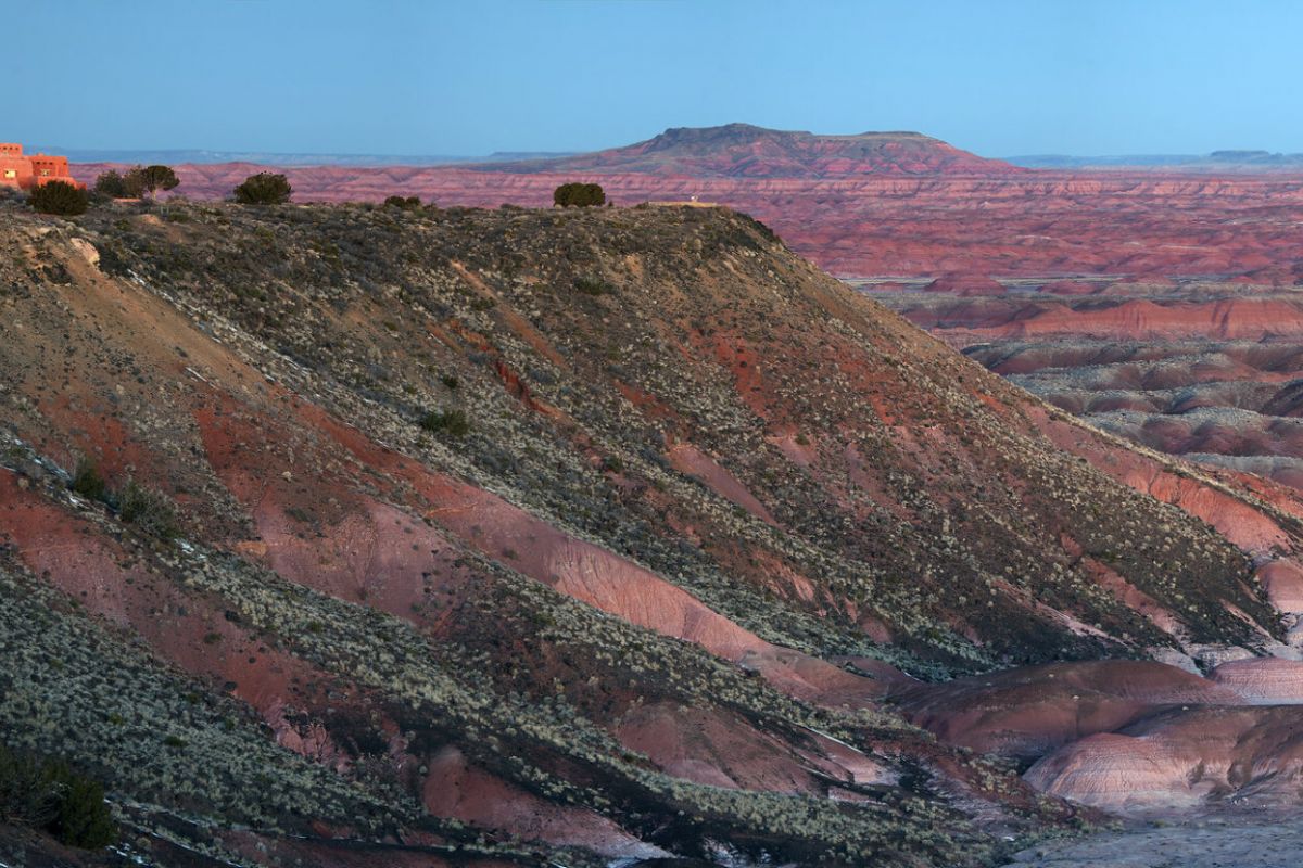 A building sits atop a cliff overlooking the colorful striped hills of Petrified Forest National Park at sunset.