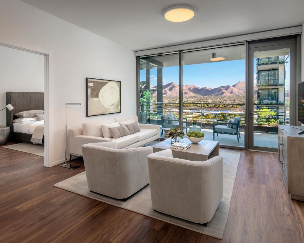 Modern living room with neutral furniture, large windows, mountain views, and an adjacent bedroom.