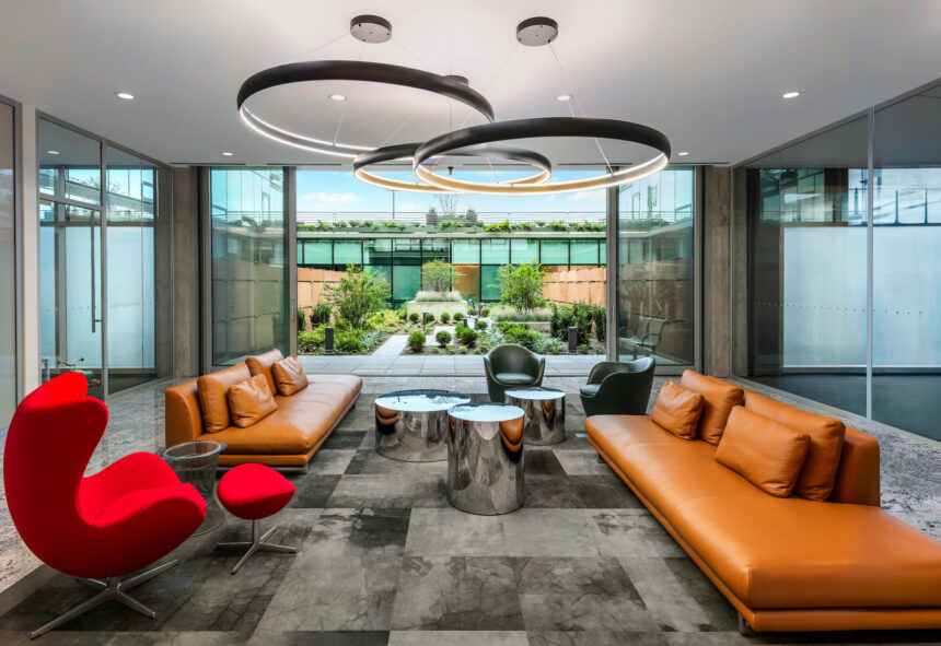 Modern office lounge with orange sofas, red chair, and circular tables—an inviting space shaping sustainable futures by the garden view.