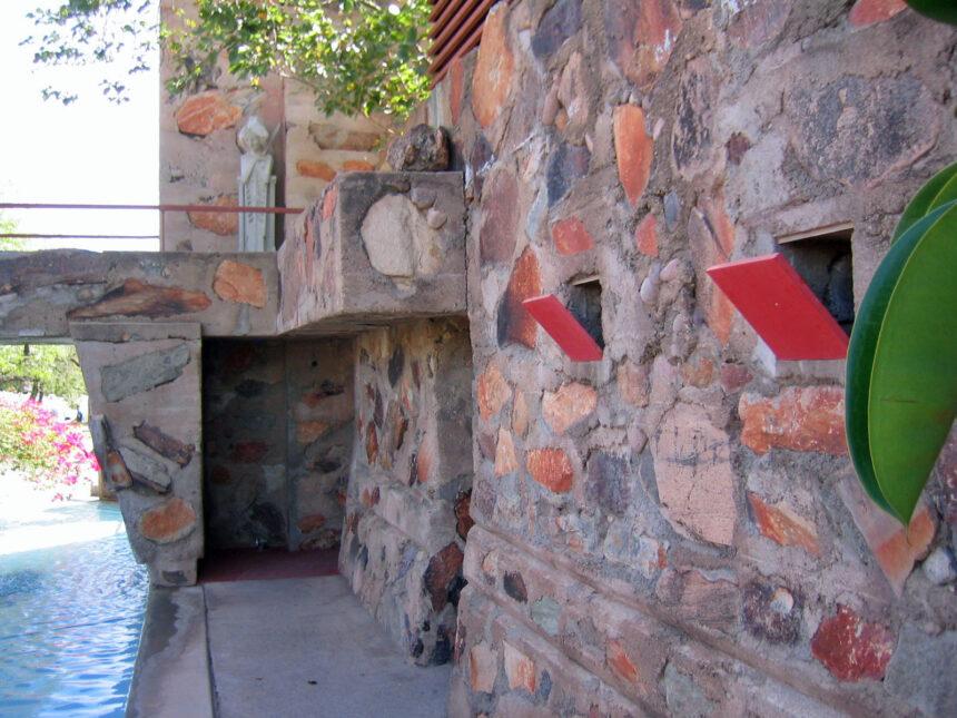 Stone wall with red arrow accents beside a narrow pool and greenery under sunlight—perfect for a Scottsdale travel photo.