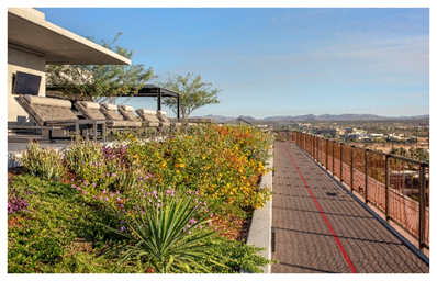 Rooftop garden with lounge chairs and a running track, where you can live Optima overlooking the city and distant mountains under a blue sky.