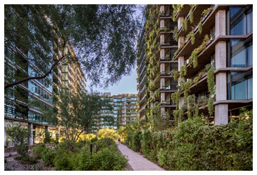 Modern apartment buildings with greenery on balconies and a pathway lined with lush plants between them.