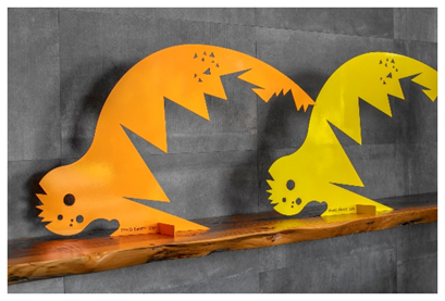 Two colorful, jagged-edged metal animal sculptures on a wooden shelf against a gray wall.