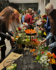 People arranging colorful flowers at a table during a group indoor flower arranging activity or workshop.