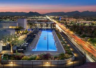 Rooftop pool overlooking a cityscape with mountains in the distance at sunset, lights glowing along the streets.