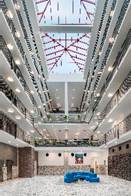 Spacious modern atrium with multiple balconies and a large skylight ceiling, featuring a blue seating area.