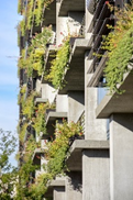 Modern concrete building with balconies, each decorated with lush green plants and flowers.