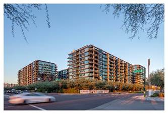 Modern apartment buildings with glass balconies along a street, with a white car driving past in the foreground.