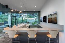 Modern kitchen with light wood bar, orange chairs, large windows, and two wall-mounted TVs.