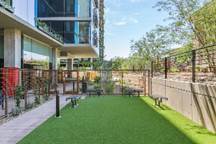 Outdoor fenced dog park area with artificial grass beside a modern apartment building.