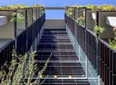 Modern building facade with glass and black panels, featuring greenery on balconies against a blue sky.