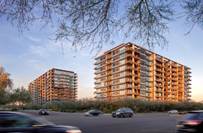 Two modern, glass-paneled apartment buildings at sunset with cars passing in the foreground.