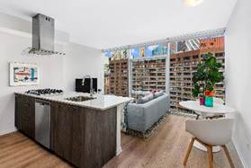 Modern apartment with open kitchen, small dining table, and living area by large windows with city views.
