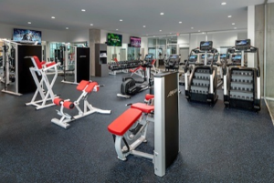 Modern gym with various exercise machines, red benches, treadmills, and weights in a spacious, well-lit room.
