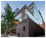 Modern brick and glass building with trees and pedestrians on the sidewalk.