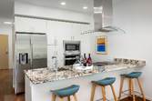 Modern kitchen with white cabinets, stainless steel appliances, and three blue stools at a marble island counter.