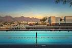 Outdoor swimming pool with lane dividers, city buildings, and mountains in the background at sunset.