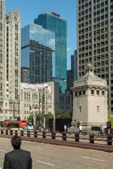 A person stands on a city street with tall buildings, enjoying the benefits of a short commute under a clear blue sky.