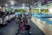 Row of stationary bikes in a modern gym with large windows overlooking a pool and greenery outside.