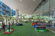 Outdoor gym area with artificial grass, workout equipment, and glass wall near modern buildings.
