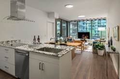 Modern apartment with a granite kitchen island, living area, large windows, and balcony view of city buildings.