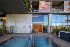 Modern outdoor pool and hot tub with glass doors and balconies reflecting the sky, located at a contemporary apartment building.