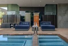 Two blue outdoor lounge chairs sit by a modern pool, surrounded by sleek glass and stone architectural features.