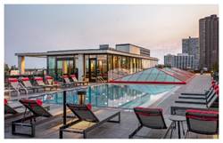Rooftop pool with lounge chairs and city buildings in the background at sunset.