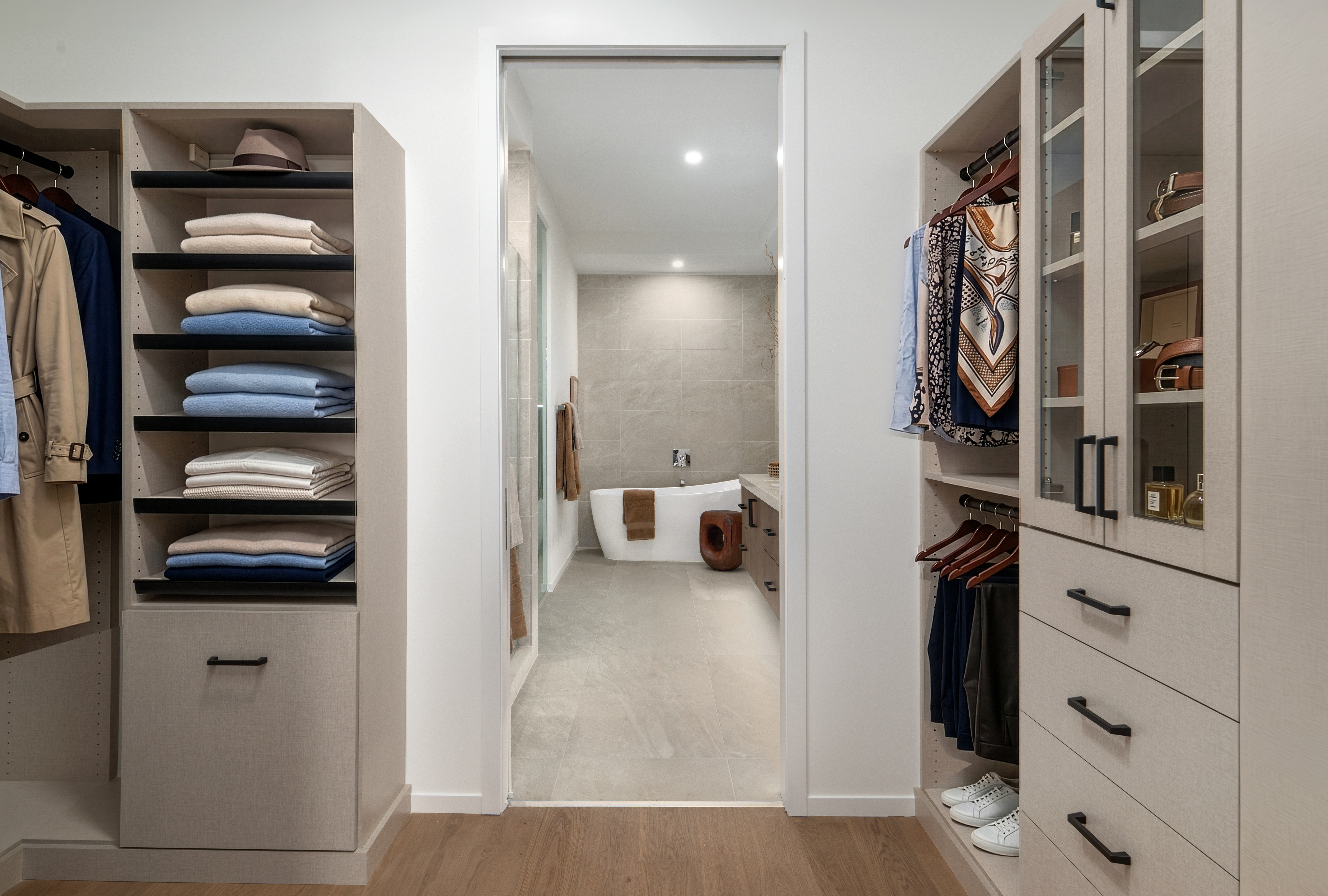 Walk-in closet with shelves and drawers leads to a modern bathroom; an optimized service is reflected in the seamless, neutral decor.